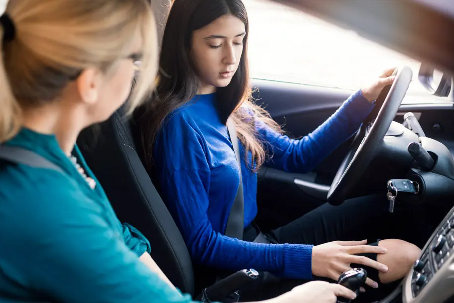 A parent and teenage driver together beside the car