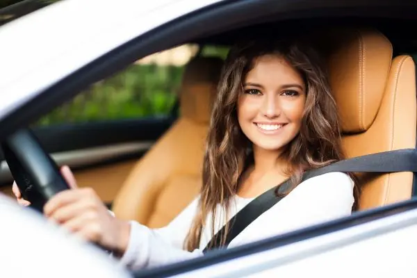 A young driver at the wheel, belted in and looking across at the instructor