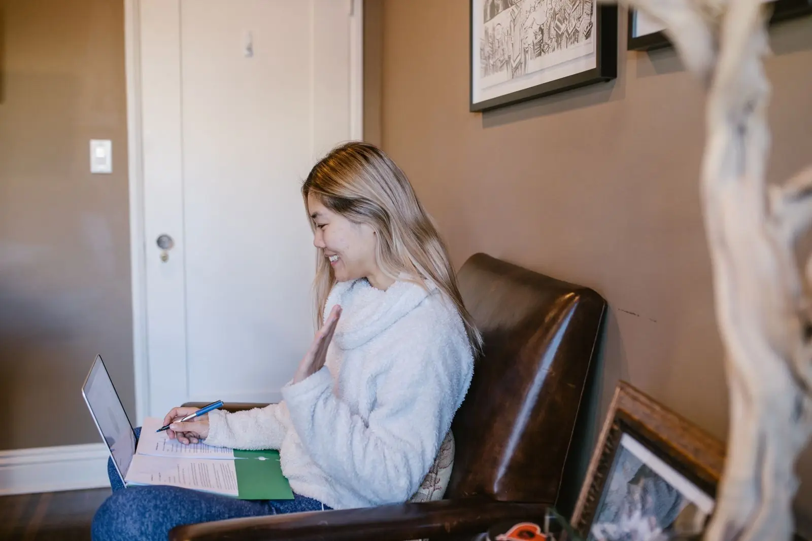 A student smiling during an online lesson with notes and a laptop