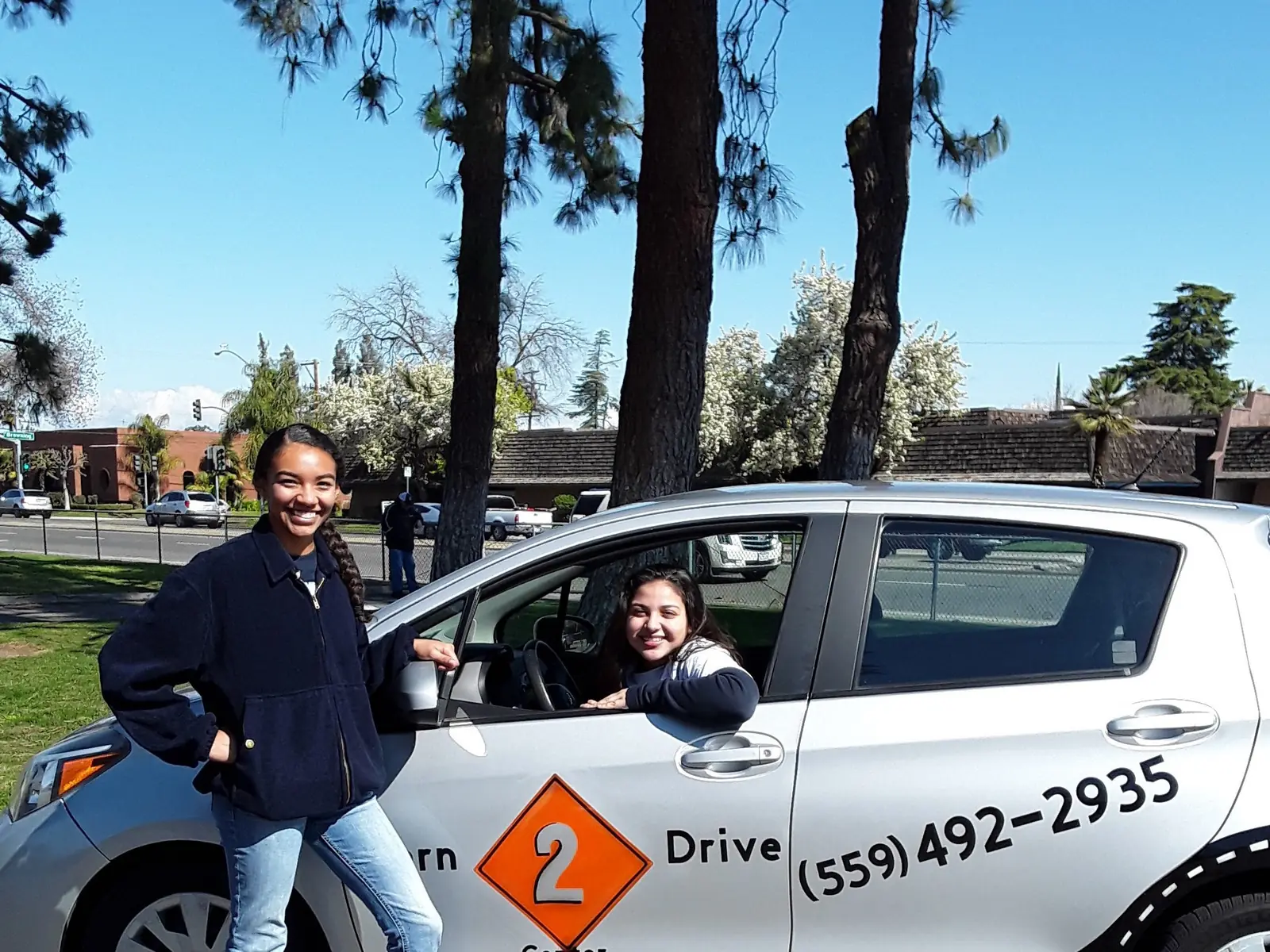Two Learn 2 Drive students beside the school car on a Fresno street in spring
