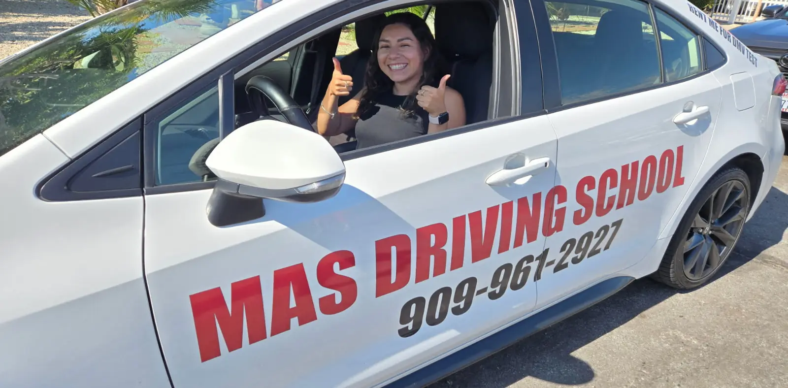 A MAS student giving a double thumbs-up from the driver’s seat of the school car