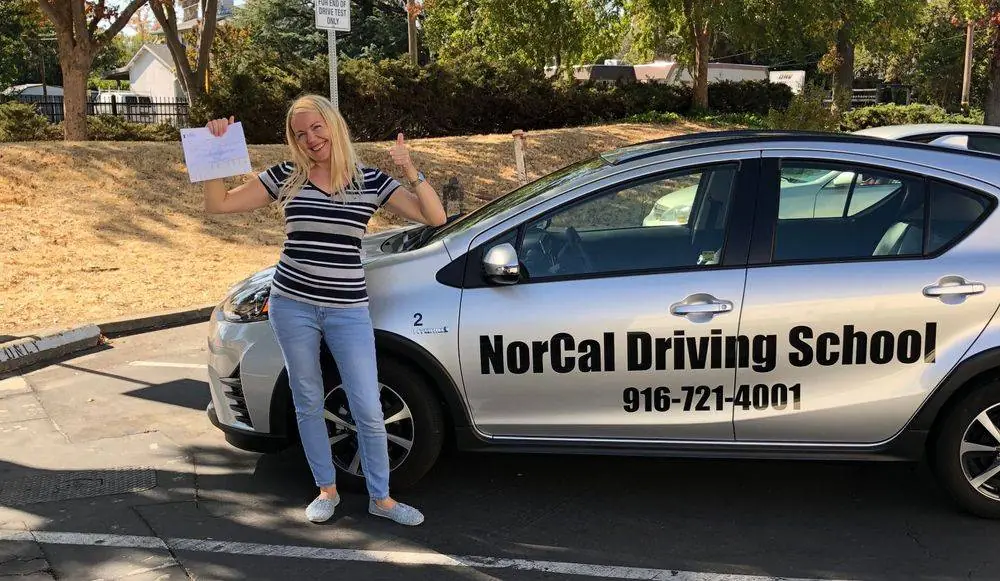 A NorCal student holding up her passed drive-test sheet beside the school car